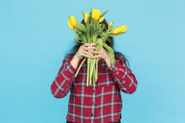 Bayram, çiçekler ve insanlar kavramı - komik kızla buket lale mavi bir arka plan üzerinde poz ellerinde ekose gömlekli