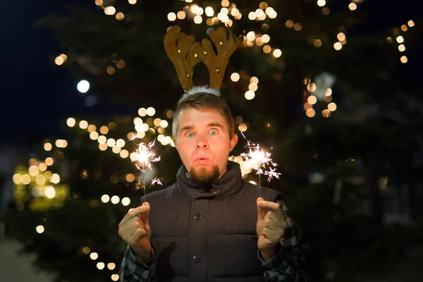 Gente, vacaciones y el concepto de Navidad - hombre sorprendido en cuernos de ciervos sosteniendo dos bengalas luz o bengalas al aire libre — Foto de Stock