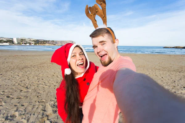 Vakantie, familie en Kerstmis concept - gelukkige paar in kerst kostuums op het strand — Stockfoto