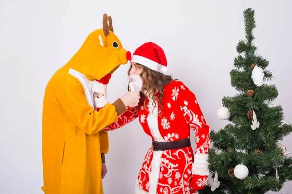 Vacances, Noël et concept de blague - Homme drôle en costume de cerf et femme en costume de Père Noël près de l'arbre de Noël sur fond blanc — Photo