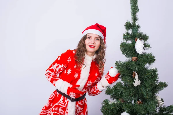Ünnep, a karácsony és a szórakozás koncepció - vicces nő fehér háttér a karácsonyfa közelében Santa Claus jelmez — Stock Fotó
