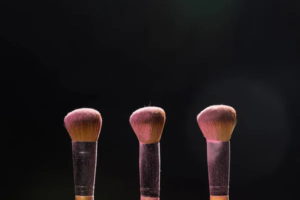 Maquillaje, belleza y concepto cosmético mineral - pinceles con polvo rosa sobre el fondo negro — Foto de Stock