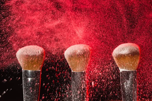 Maquiagem, beleza, conceito cosmético mineral escova de pó no fundo preto com pó vermelho salpicado sobre ele — Fotografia de Stock