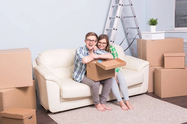 Home, relocation and moving concept - happy couple in glasses holding a card board and sitting on sofa