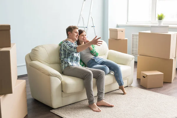 Furniture, moving and people concept - happy couple sitting on new sofa in an empty apartment among boxes and argue about something