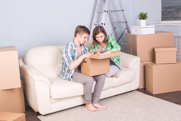 Дом, люди и движущаяся концепция - молодая пара ищет что-то в коробке, сидя на диване — стоковое фото