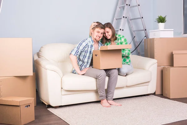 Conceito imobiliário, de realocação e de mudança - jovem casal segurando um papelão sentado no sofá — Fotografia de Stock