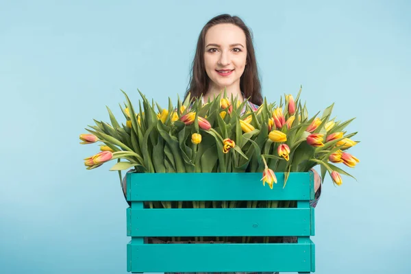 행복 한 백인 여성 꽃집 웃으면서 파란색 배경에 튤립의 큰 상자를 들고 — 스톡 사진