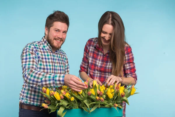 Happy floristas fixando tulipas em uma grande caixa de madeira no fundo azul — Fotografia de Stock