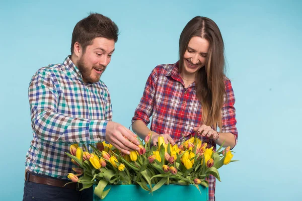 Feliz homem e mulher floristas segurando caixa com tulipas e rindo no fundo azul — Fotografia de Stock