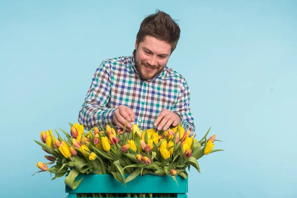 Hombre guapo fijando un ramo de flores sobre fondo azul — Foto de Stock