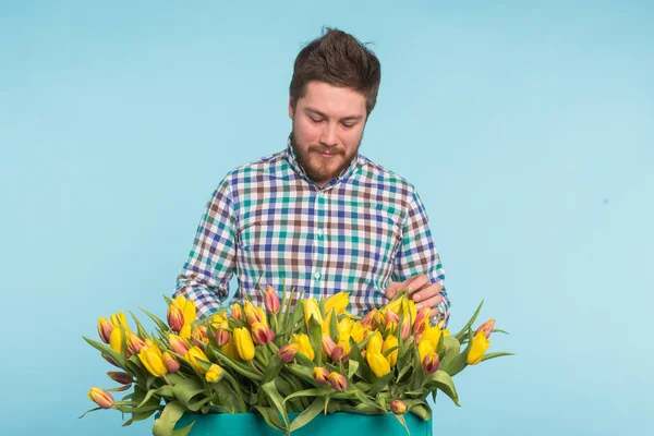Cheerful handsome man florist with box of tulips on blue background