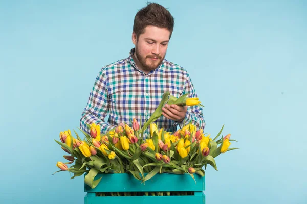 파란색 배경에 꽃의 꽃다발을 고정 하는 잘생긴 남자 — 스톡 사진