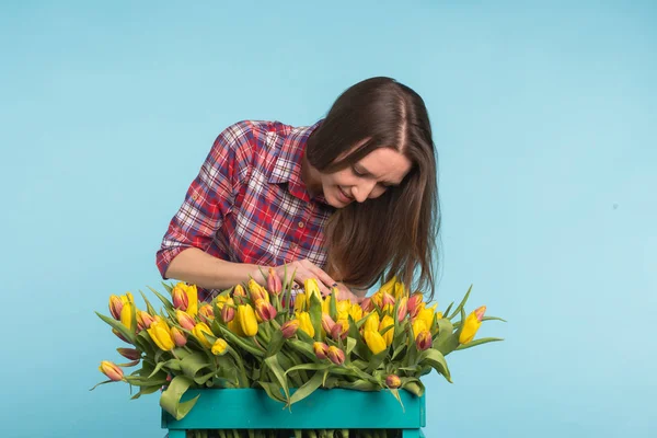 Charming female florist sorts out tulips in the box, selects them for the future flower arrangement