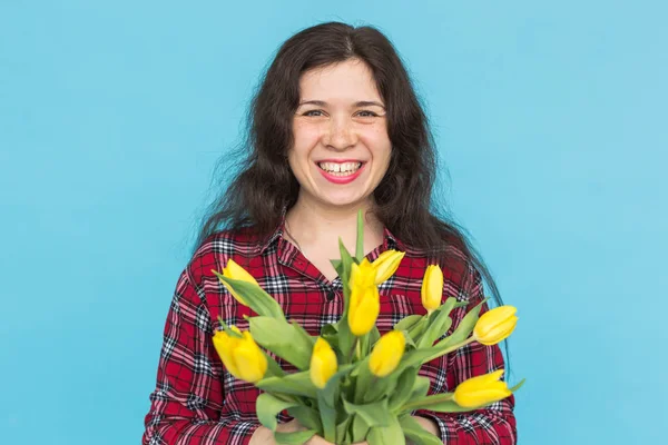 Vacances, fleurs et concept de personnes - Funny girl en chemise à carreaux avec bouquet tulipes dans les mains posant sur un fond bleu — Photo