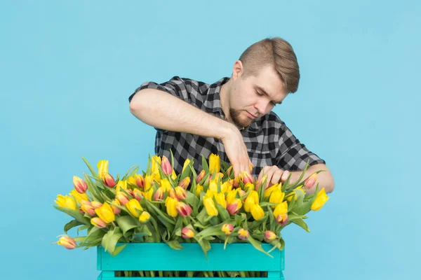 Handsome white male gardener making a bouquet of tulips in blue studio.