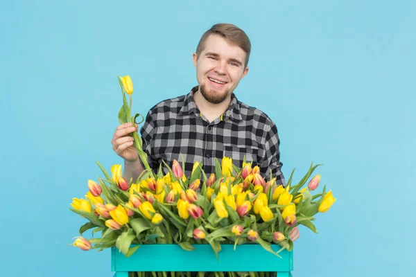 Florística, férias e conceito de pessoas - Jardineiro homem que fixa um buquê de tulipas no fundo azul . — Fotografia de Stock