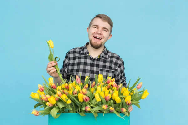 Handsome white male gardener making a bouquet of tulips in blue studio.