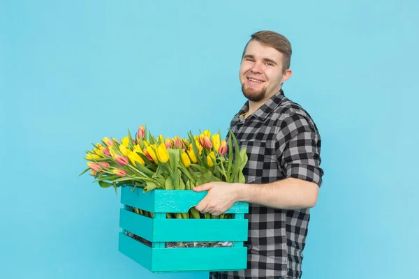 Jardineiro masculino caucasiano com caixa de tulipas rindo em fundo azul — Fotografia de Stock