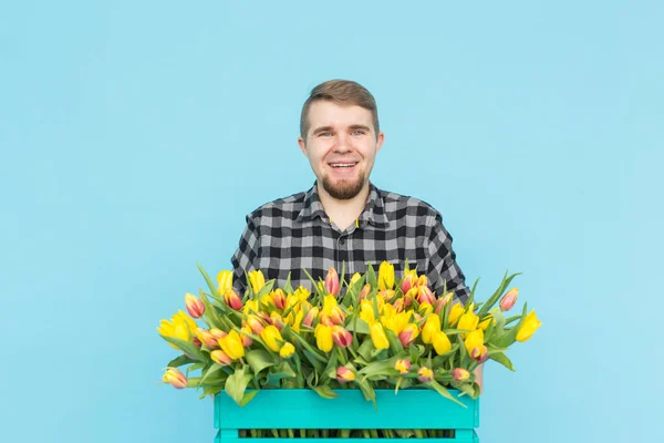 Jardineiro masculino caucasiano com caixa de tulipas rindo em fundo azul — Fotografia de Stock