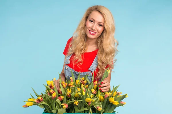 Charming blonde female florist sorts out tulips in the box, selects them for the future flower arrangement