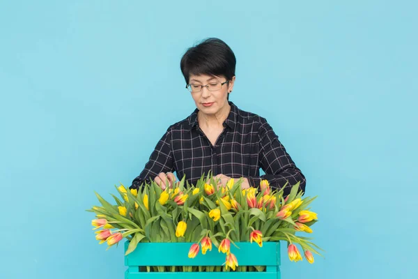 Charming brunette female florist sorts out tulips in the box, selects them for the future flower arrangement