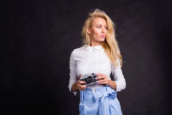 Fotograferen, mode en mensen concept - jonge blonde vrouw maken van een foto van iets en kijken naar iets in de buurt van haar op zwarte achtergrond met kopie ruimte — Stockfoto
