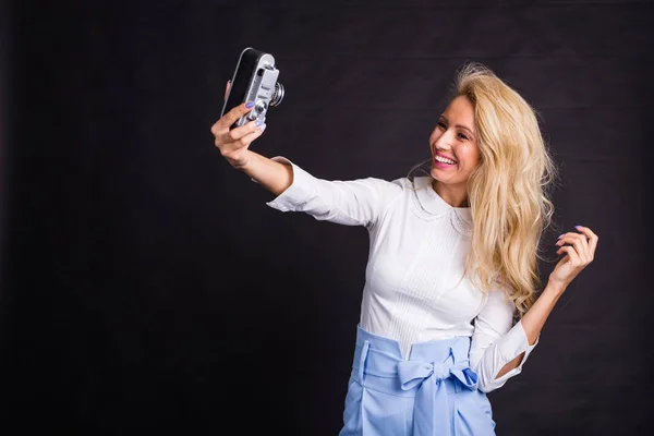 Fiatal, vonzó szőke nő vesz selfie vintage kamera fekete háttér — Stock Fotó