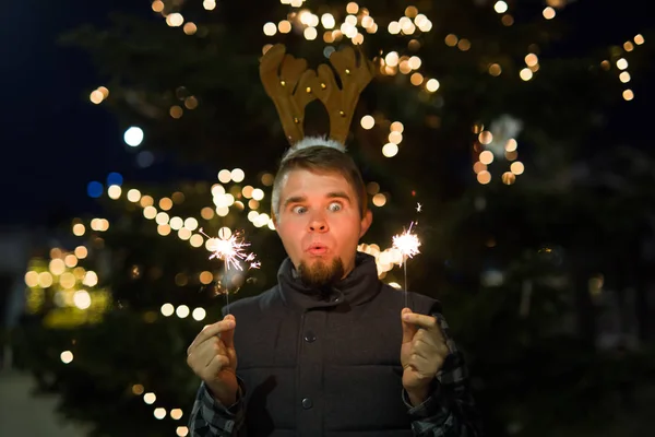 Mensen, vakantie en Kerstmis concept - grappige jongeman in Kerstmis herten kostuum met bengals licht buiten — Stockfoto