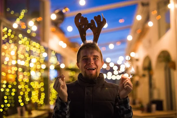 Människor, helgdagar och jul koncept - unga rolig människa i christmas rådjur kostym med bengaler ljus utomhus — Stockfoto