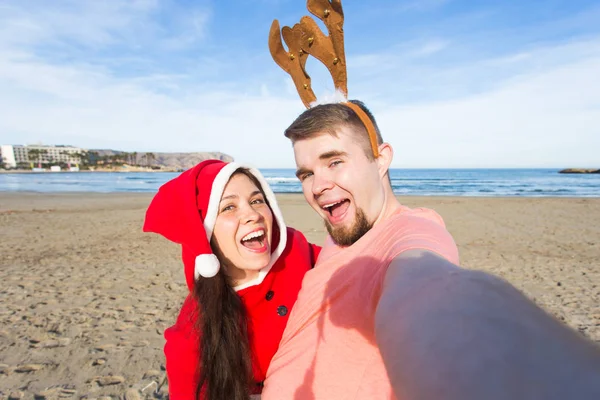 Boże Narodzenie, humor, ludzie koncepcja - Wesołych Świąt para zabawy biorąc selfie na plaży — Zdjęcie stockowe
