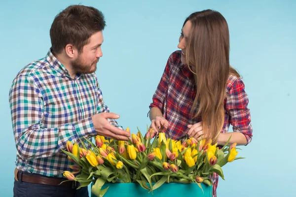 Feliz homem e mulher floristas segurando caixa com tulipas e rindo no fundo azul — Fotografia de Stock
