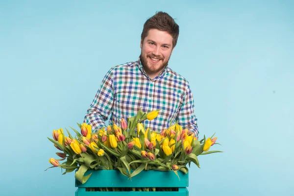 Hombre guapo fijando un ramo de flores sobre fondo azul — Foto de Stock