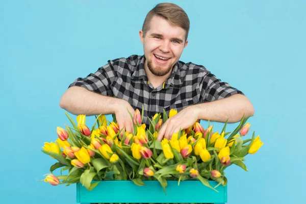 Bonito jardineiro caucasiano masculino fazendo um buquê de tulipas em estúdio azul . — Fotografia de Stock