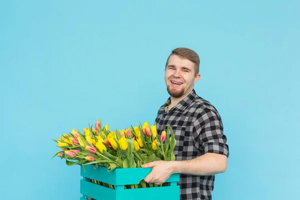 Alegre homem bonito florista segurando caixa de tulipas no fundo azul — Fotografia de Stock