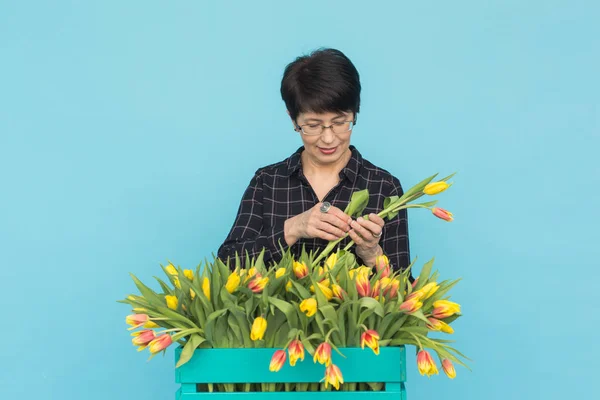 Charming brunette female florist sorts out tulips in the box, selects them for the future flower arrangement