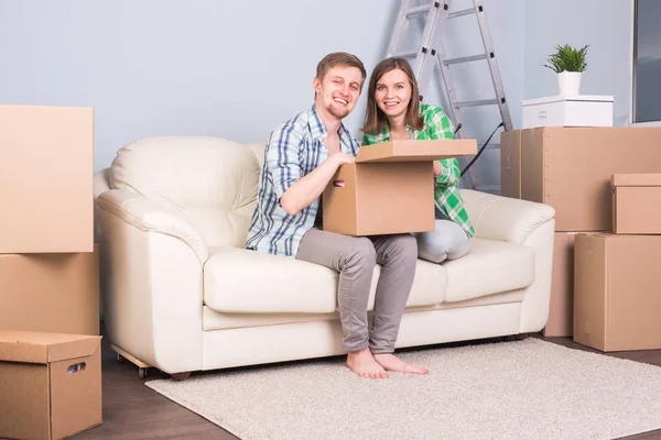Mudança, novo conceito de apartamento e realocação - casal feliz abrindo sua caixa juntos por causa de se mudar para um novo apartamento — Fotografia de Stock