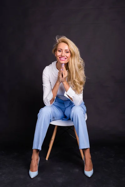 Atractiva mujer rubia sentada en silla sobre fondo negro — Foto de Stock