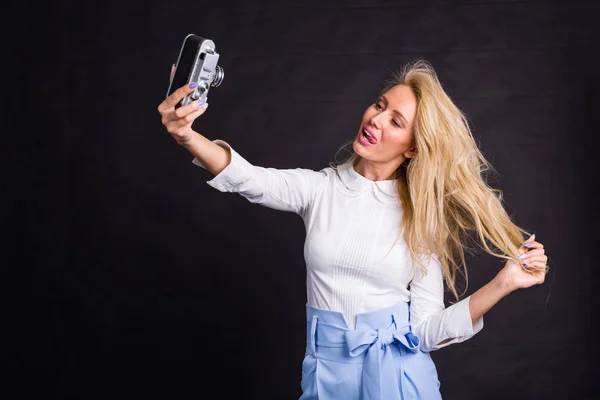 Jonge aantrekkelijke blonde vrouw nemen selfie op vintage camera op zwarte achtergrond — Stockfoto