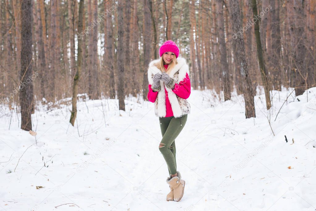 Beauty, nature and people concept - beautiful blond woman walking in pink hat and sweaters in winter wood and smiling