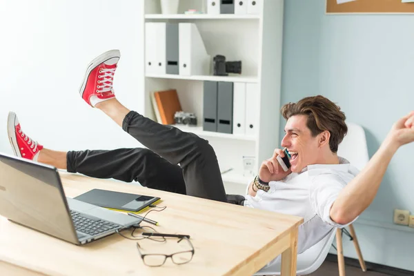 Business, people and fun concept - handsome man talking on mobile phone and puts feet up on table in the office. — Stock Photo, Image