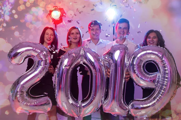 Il nuovo anno 2019 sta arrivando. Gruppo di giovani allegri che tengono numeri argentati e lanciano coriandoli sulla festa . — Foto Stock