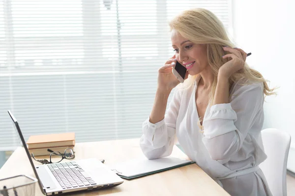 Business, technologie et concept de communication - femme blonde parlant téléphone tout en regardant un ordinateur portable — Photo