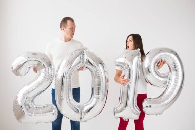 Yeni 2019 yılı önümüzdeki kavramı - şaşırmış genç adam ve kadın kapalı gümüş renkli numaraları tutuyorsun.