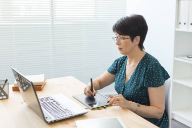 Office, grafik tasarımcı, dijital - dizüstü bilgisayar ve dijital tablet ofisinde çalışan orta yaş kadın