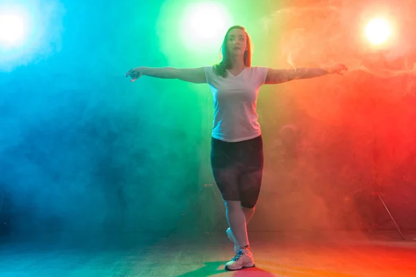 Dance, sport, and people concept - young woman dancing in the darkness under colourful light