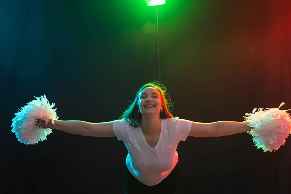 Concepto de danza, deporte y gente: una hermosa joven bailando en la oscuridad con pompones y sonriendo — Foto de Stock