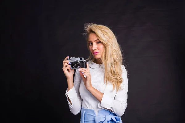 Mode, vrije tijd en mensen concept - jonge blonde vrouw maken van een foto en glimlachend op zwarte achtergrond met kopie ruimte — Stockfoto