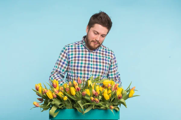 Hombre guapo fijando un ramo de flores sobre fondo azul — Foto de Stock