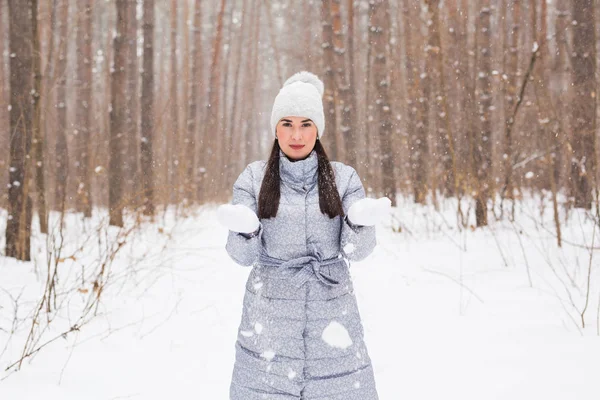 Winter, season and people concept - Woman in grey coat and white hat walking in winter park and playing with snow — Stock Photo, Image